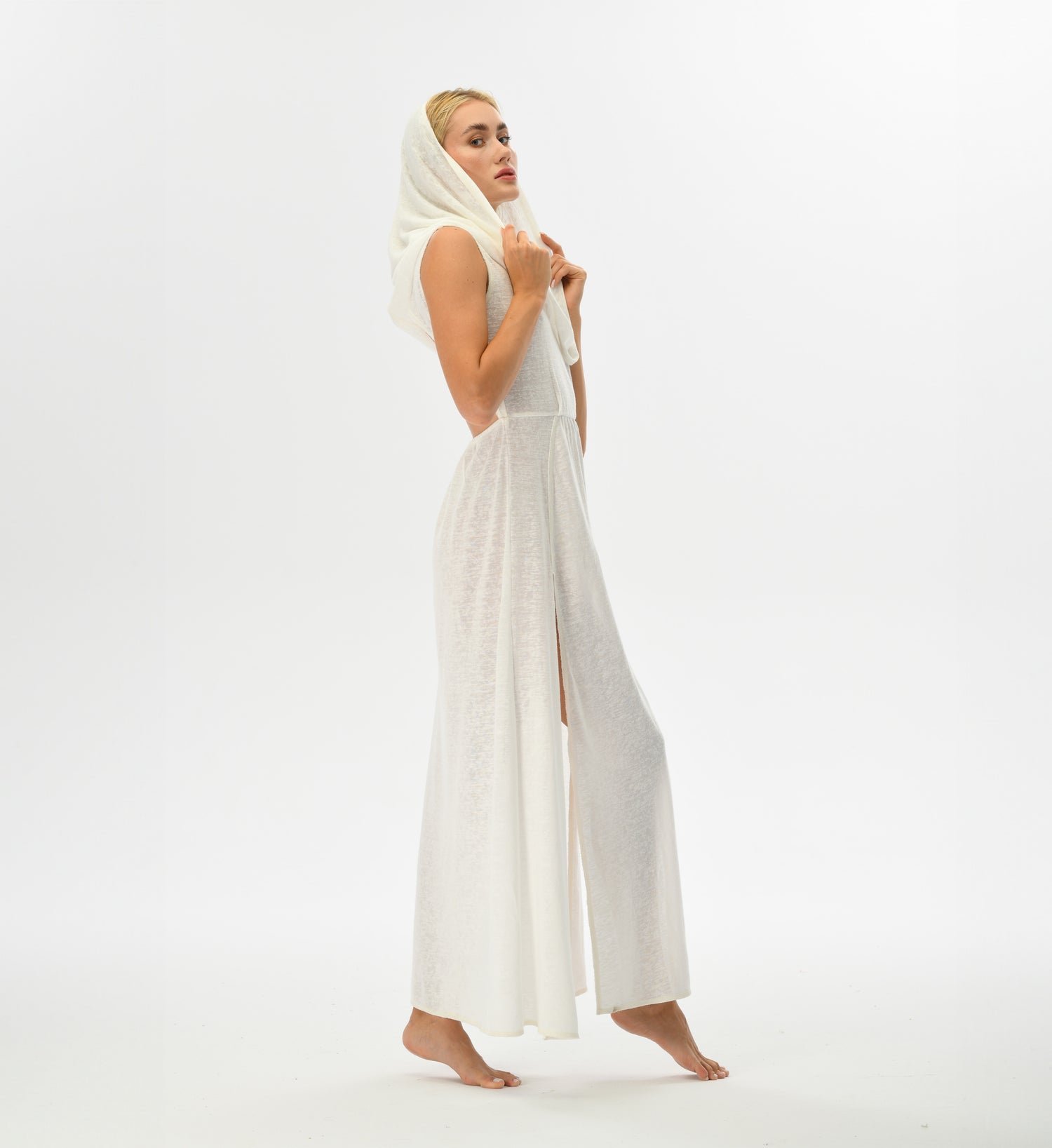 Warrior-inspired white dress with an open back, high side splits, and a hood that transforms into a shawl. Made from a hand-dyed cotton and linen blend, ideal for festival fashion.