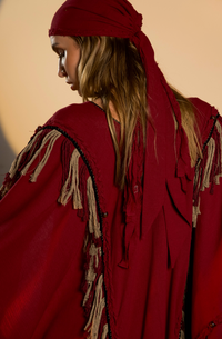 Women’s red boho poncho coat, made from organic cotton with braids and fringes. Fits XS to XXL, ideal for layering at festivals and casual outings.