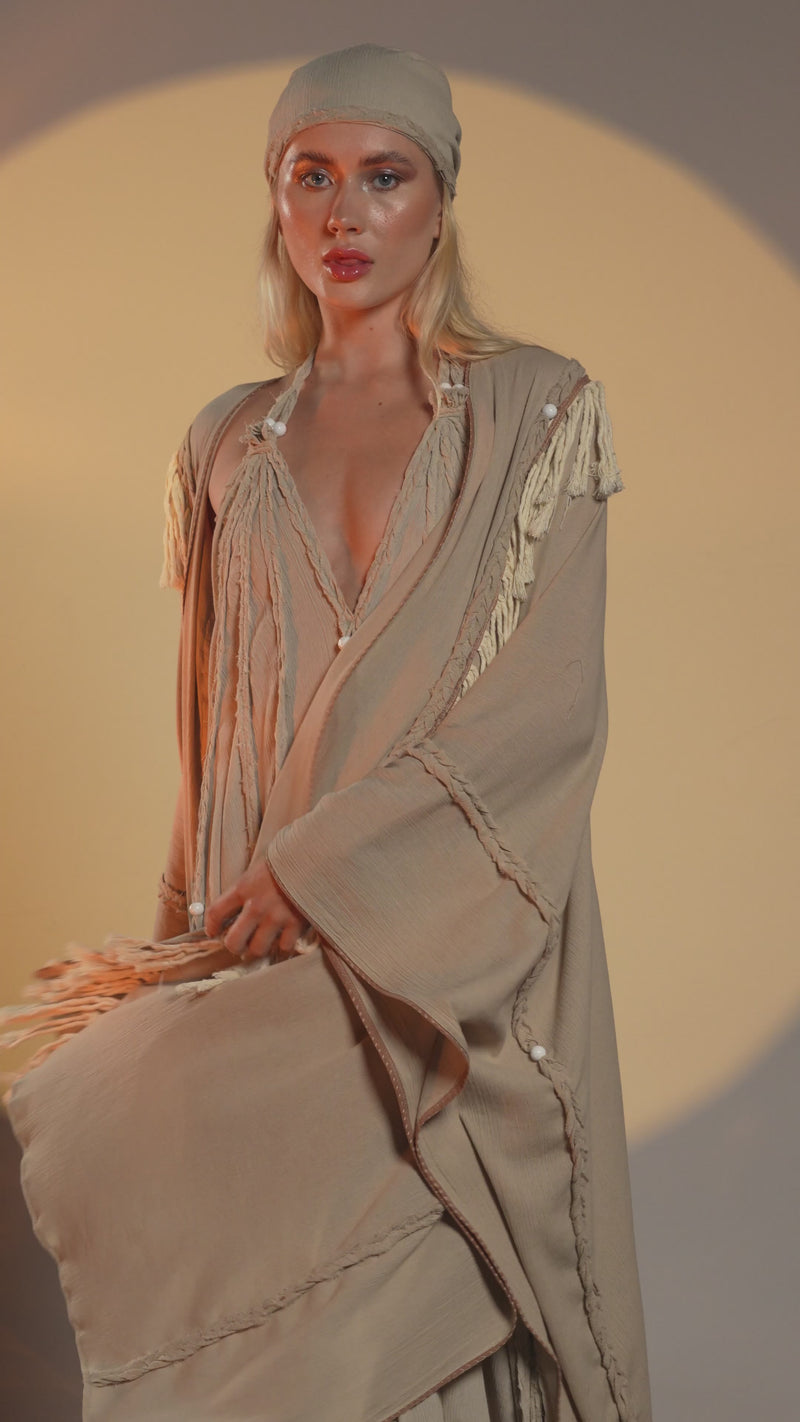 Beige boho cape with handmade fringe and braids, made from organic cotton, ideal for shamanic-inspired festival wear or casual bohemian outfits.